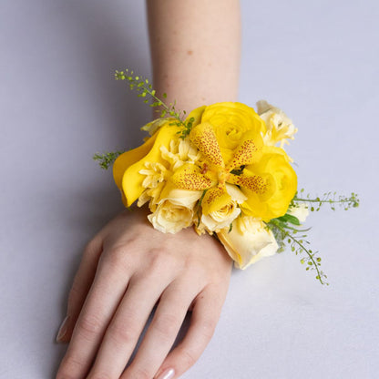 Yellow floral wrist corsage on a person's wrist against a light gray background
